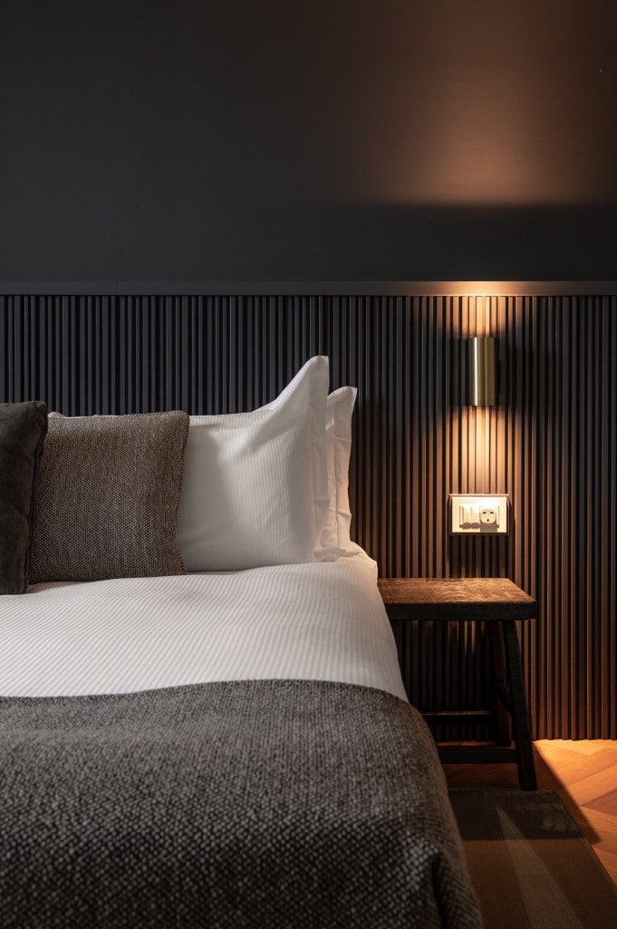 Bedroom with dark fluted panel headboard, brass wall sconce and herringbone parquet floor