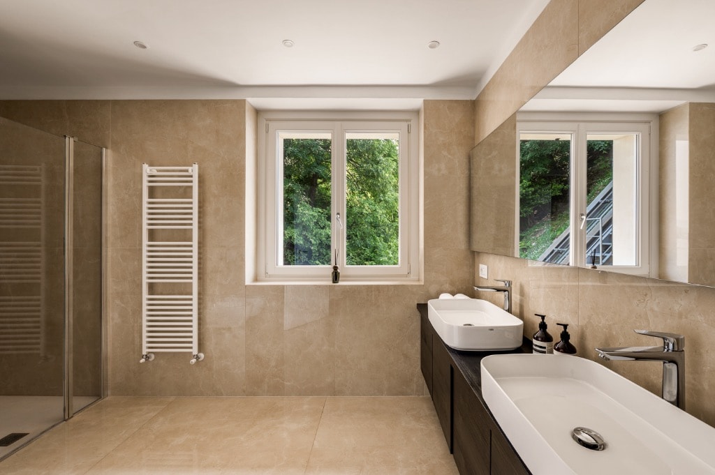 Bathroom with travertine tiles, double vanity and garden-view windows